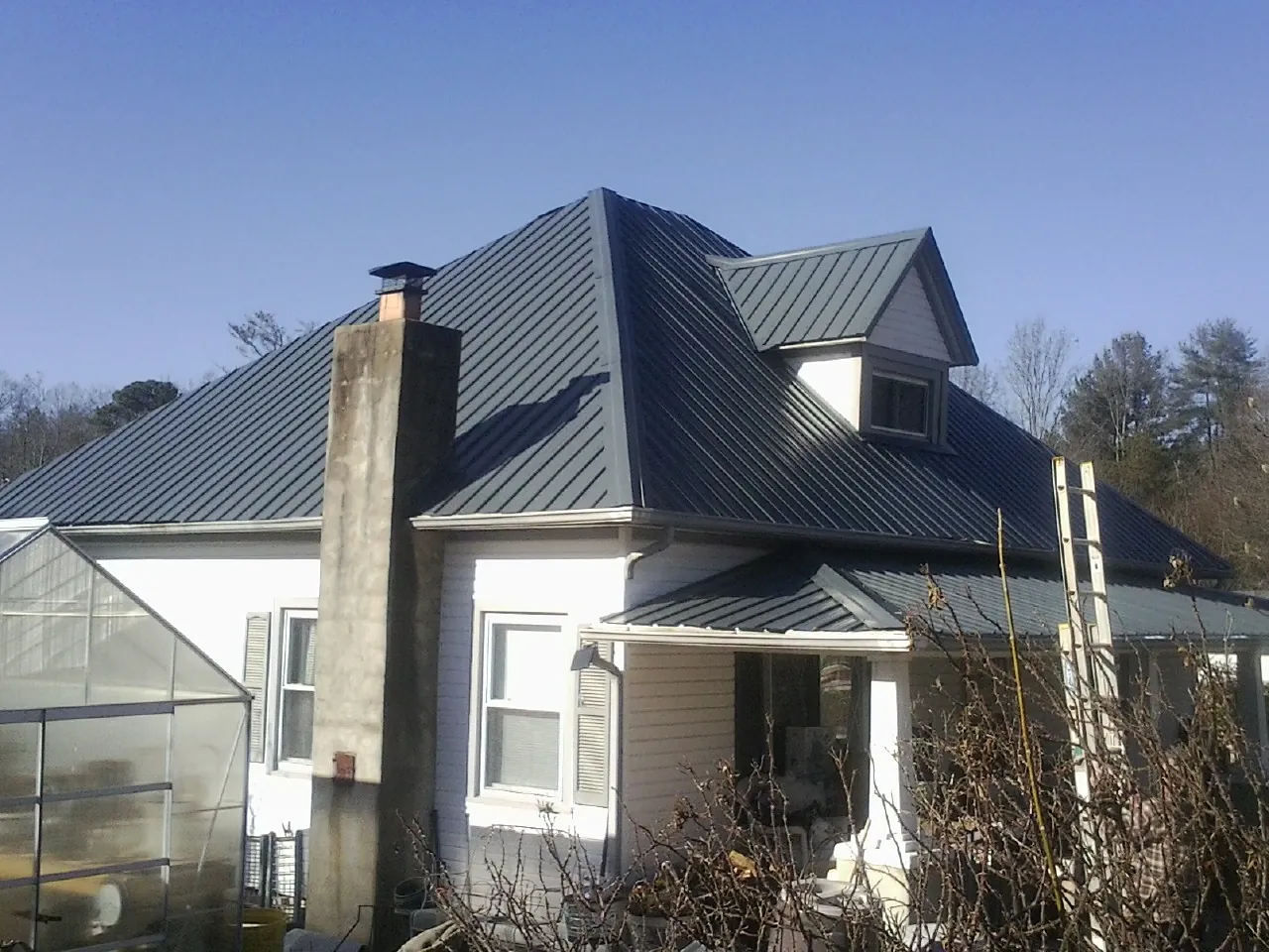 Dark blue standing seam metal roof on a white farmhouse with dormer — Slate & Tile Roof Repair by Roofing Brothers in Saint Helena