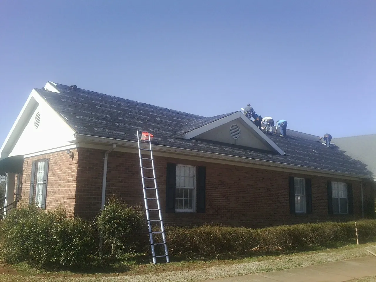 Crew tearing shingles off a brick ranch roof with a ladder set — Emergency Roof Repair work by our crew in Saint Helena