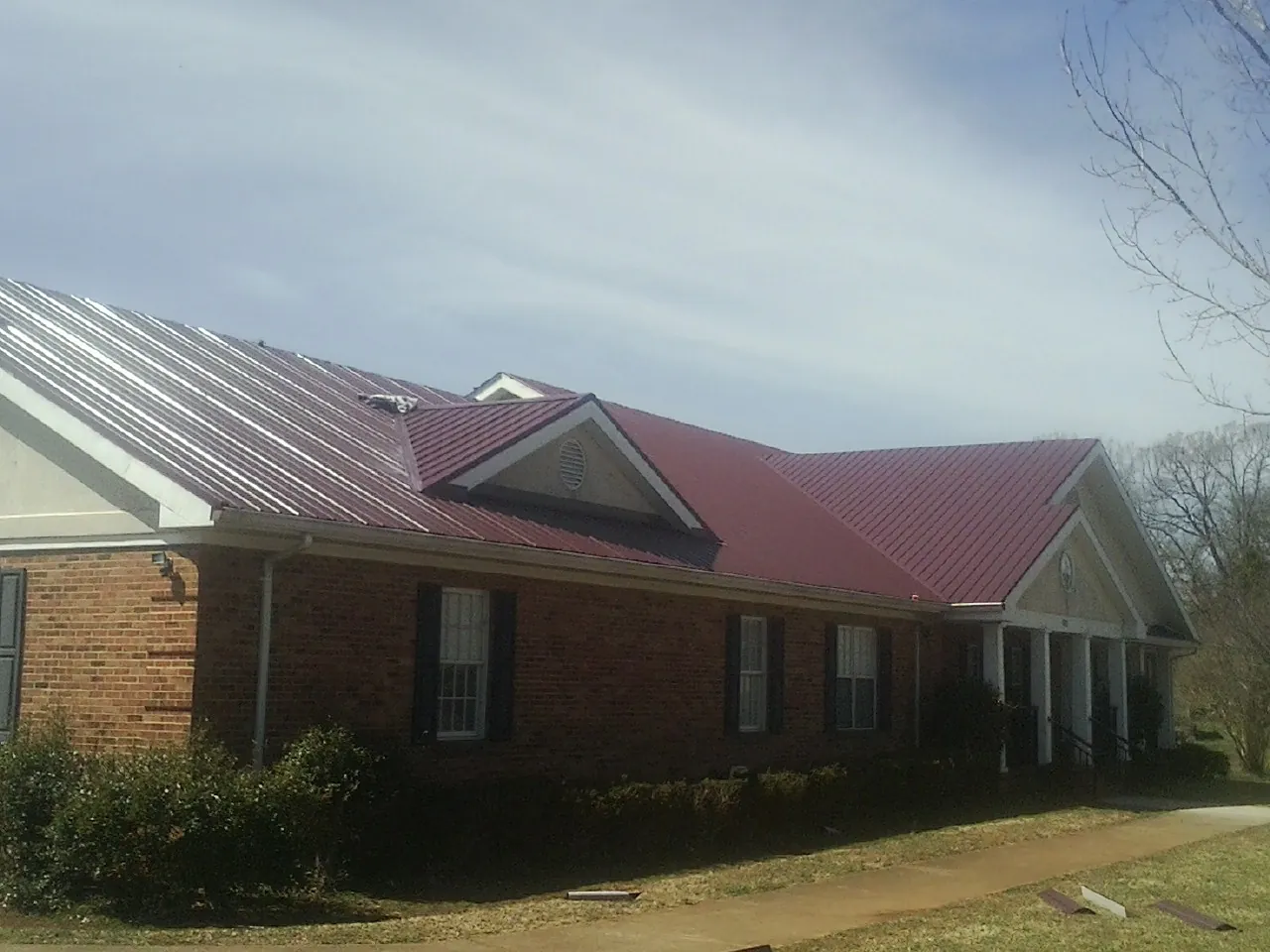 Red metal roof with gabled entries on a long brick building, from a Hail Damage Roof Repair job in Saint Helena